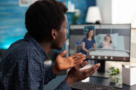 African american man checking on family in hospital ward using online intenet video call to talk with relatives. Black person understanding child diagnosis from mom and girl at clinic