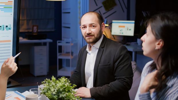 Portrait of smiling businessman looking into camera working at company strategy in business meeting office room late at night. Diverse multi-ethnic collegues discussing marketing expertise overtime