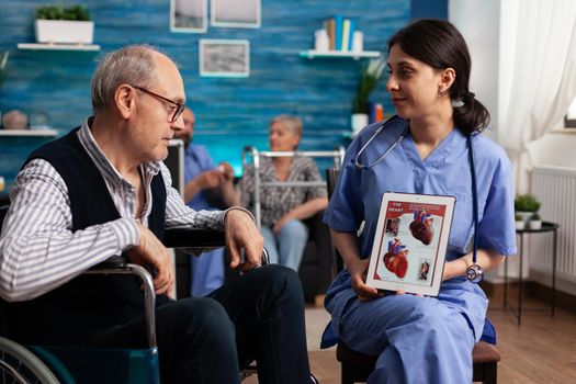 Social nurse worker explaining heart cardiogram radiography to retired disabled senior man using tablet computer. Social services nursing elderly retired male. Healthcare assistance