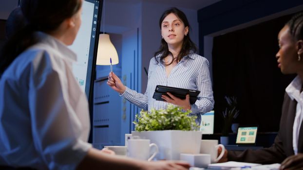 Overworked focused diverse businesspeople working in business company meeting office room brainstorming marketing strategy late at night. Entrepreneur woman presenting financial ideas