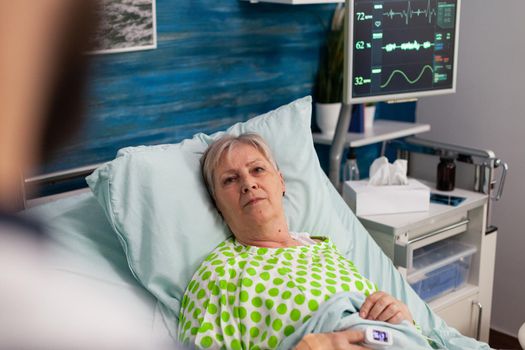 Disabled pensioner woman lying in bed discussing medical treatment with man assistant caregiver during healthcare recovery. Social services nursing elderly retired female. Healthcare assistance