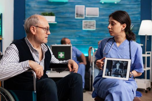 Social nurse worker explaining medical radiography using tablet computer to pensioner disabled senior man patient. Social services nursing elderly retired male. Healthcare assistance