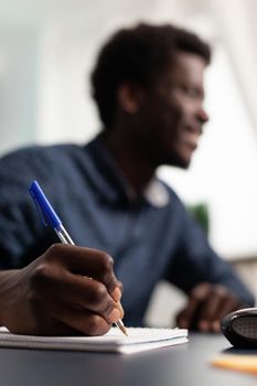 Black business student taking notes on notebook using computer, remote working from home and taking online college classes. African american man learning lessons on internet connection