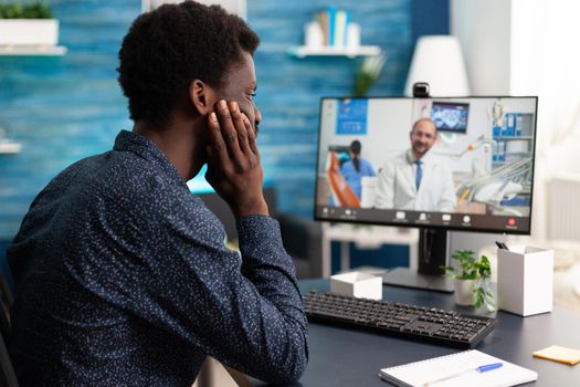 Healthcare consultation of african american guy talking to doctor using video call app sitting at home. Sick patient black man doing virtual telemedicine for disease cure and treatment