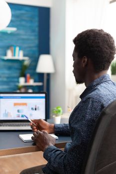 Black man working from home using financial economy data app on laptop. African american guy computer user using business workplace internet online website communication job lifestyle