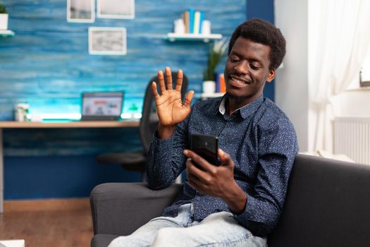 Black man greeting colleagues on video call conference in living room. Working from home african american remote worker in distance communication chat, learning about business project