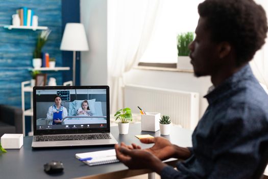 Father on online video call via laptop, talking with doctor from hospital ward about child healthcare, using internet telemedicine app and technology consultation for treatment and diagnose