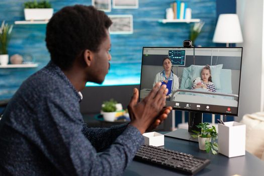 Worried black dad for her little girl in hospital ward talking with doctor on video call using computer webcam for family meeting. Medic consultation via online internet connection