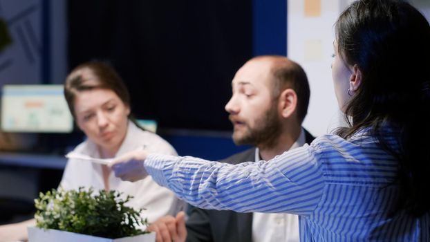 Selective focus of businesswoman discussing financial graphs analyzing company statistics paperwork working in office meeting room late at night. Multi-ethnic teamwork brainstorming ideas