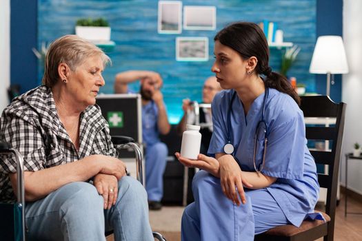 Assistant woman helper explaining pills treatment discussing with senior elder person with disability during social services. Healthcare assistance. Social services nursing at home