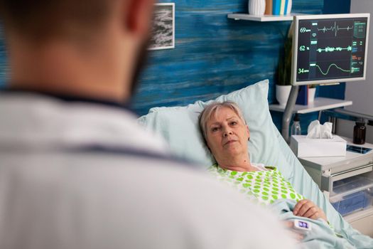 Disabled pensioner woman lying in bed discussing medical treatment with man assistant caregiver during healthcare recovery. Social services nursing elderly retired female. Healthcare assistance