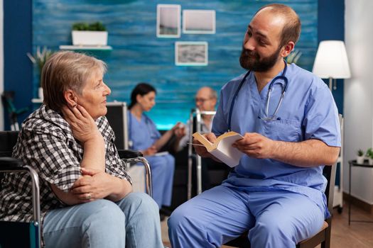 Caregiver support nurse reading book stories to senior disabled pensioner woman in living room. Social services nursing elderly female. Healthcare assistance. Disability people support