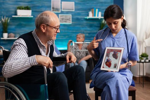 Social nurse worker explaining heart cardiogram radiography to retired disabled senior man using tablet computer. Social services nursing elderly retired male. Healthcare assistance