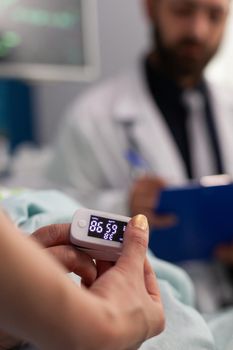 Asisstant nurse puts medical oximeter on finger while doctor man writes heartbeat puls rate on clipbord during consultation. Social services nursing elderly retired female. Healthcare assistance