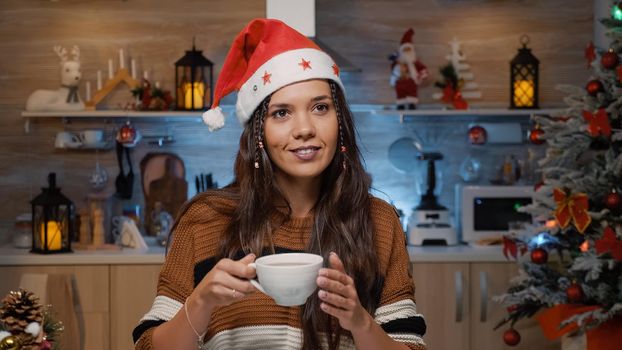 Cheerful festive woman smiling because of winter season while holding cup of tea in christmas decorated kitchen at home. Person thinking about festivity dinner gathering with friends