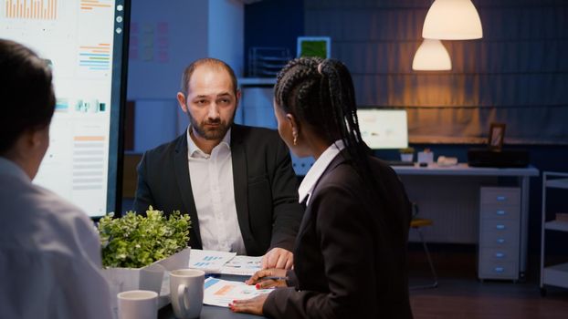 Multi ethnic teamwork entering in business office meeting room discussing company strategy analyzing management graphs late at night. Diverse coworkers brainstorming corporate ideas