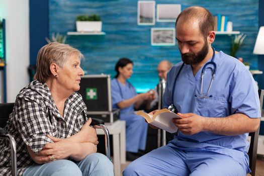 Caregiver support nurse reading book stories to senior disabled pensioner woman in living room. Social services nursing elderly female. Healthcare assistance. Disability people support