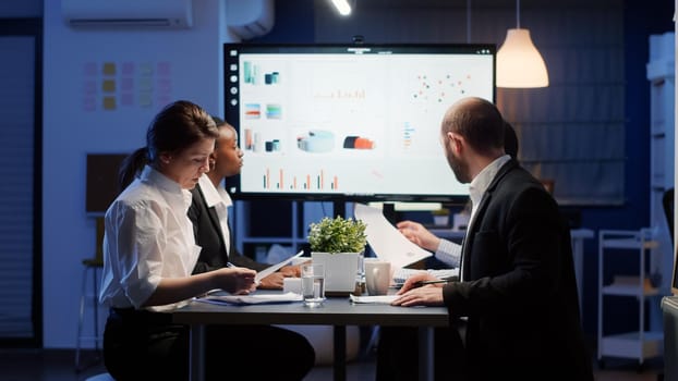 Diverse group of businesspeople looking at management strategy presentation on monitor brainstorming ideas. Multi ethnic teamwork working in office meeting room solving corporate solution