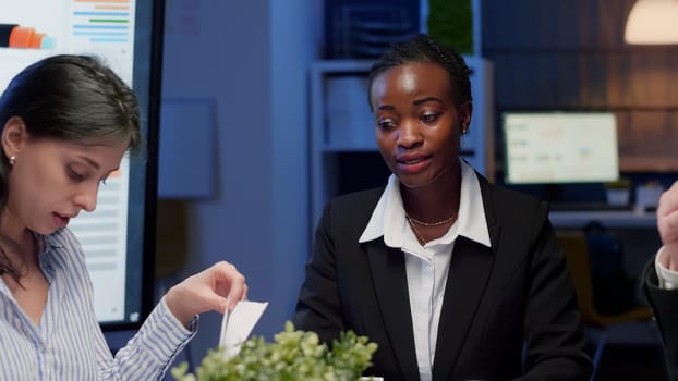 African american businesswoman brainstorming business strategy working in meeting room late at night. Diverse multi ethnic teamwork planning company management presentation working at ideas