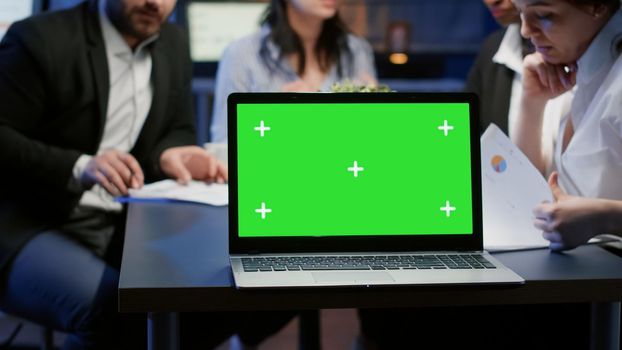 Diverse multi ethnic teamwork brainstorming company ideas working in business meeting office late at night. Mock up green screen chroma key with isolated display standing on table conference