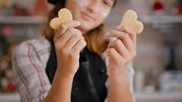 Selective focus of grandchild holding cookie dough with heart shape in hands enjoying cooking traditional homemade traditional. Child preparing xmas delicious dessert during christmas holiday