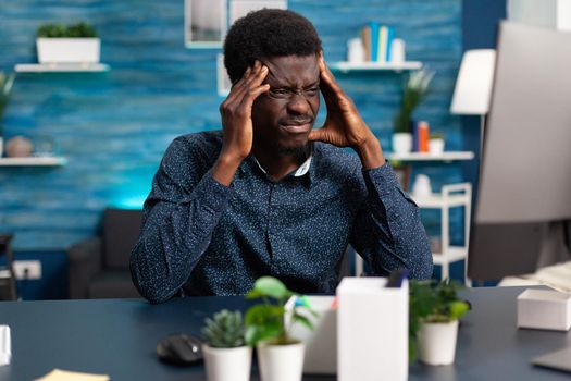 Sick african american guy stressing about deadline project having big headache. Exhausted black man worrying about business while working from home in cozy flat. Tired overwhelmed person