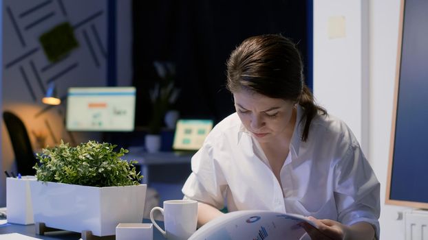 Focused businesswoman working hard overtime in business office meeting room late at night analyzing management graphs while drinking coffee. Entrepreneur woman analyzing company profit