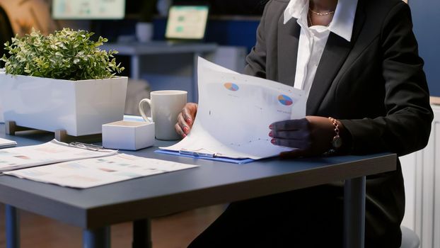 Focused black african american businesswoman working overtime at company management presentation late at night in office meeting room. Executive manager analysing financial profit paperwork