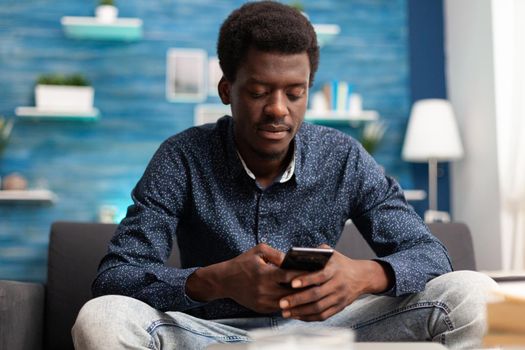 African american guy on video call using smartphone in living room. Online black person working from home for office virtual communication and business project planning on digital technology