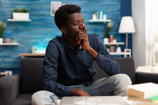 Portrait of stressed, pensive african american man looking out the window thinking about business problems. Adult man in living room working from home office desk. Serious black person