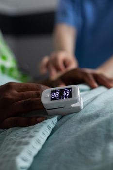 Close up of oximeter on african american girl hand laying in hospital ward bed. Device showing low oxygen saturation and pressure measurement used on young patient with disease. Medical equipment