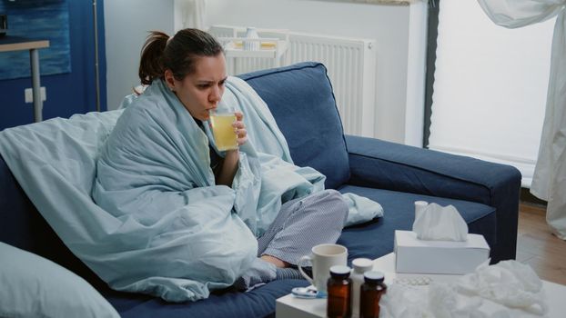 Woman with flu drinking effervescent medication with water to cure cold and disease. Sick adult holding glass with vitamin beverage while having headache and temperature. Unwell person