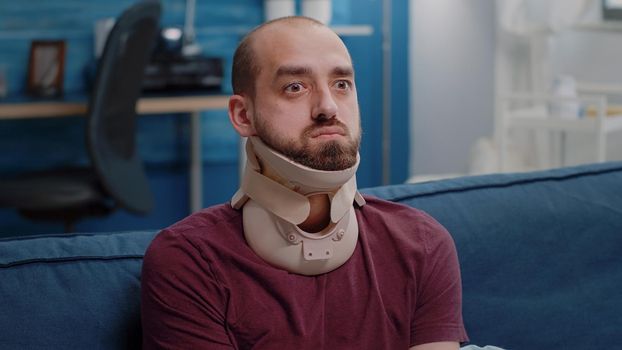 Close up of ill person wearing cervical neck collar against vertebra pain. Man with medical foam feeling sick while trying to heal muscle injury. Injured adult feeling unhappy