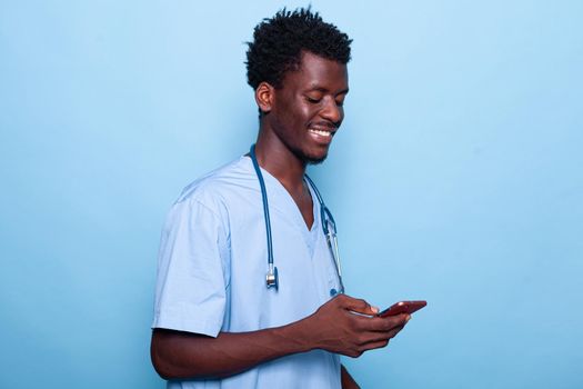 Man working as nurse looking at smartphone and smiling. Medical specialist wearing uniform and stethoscope holding modern phone with touch screen. Healthcare assistant using device