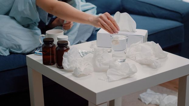 Close up of woman hand preparing effervescent drink with vitamin and medication for cold and flu treatment on table with bottles of pills, capsules and tissues. Sick person with medicament