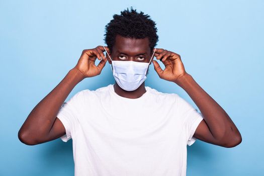 Portrait of casual man using hands to put face mask on face for protection against coronavirus pandemic. Young adult using mask for healthcare and prevention. Person looking at camera