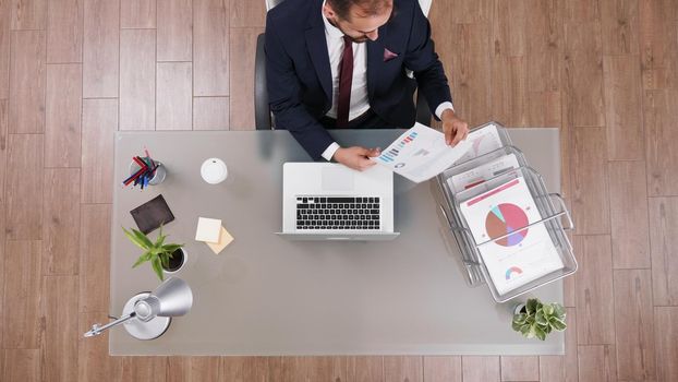 Top view of businessman analyzing company statistics documents working at financial strategy in startup corporate office. Executive director in suit analysing investments paperwork