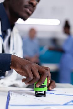 Close up of african american hand holding stamp on papers for checkup appointment and prescription medicine. Black doctor using professional office seal sitting in healthcare cabinet