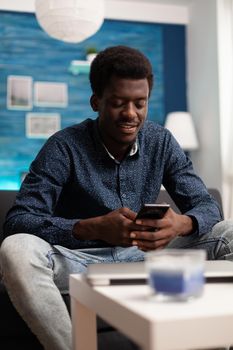African american guy on video call using smartphone in living room. Online black person working from home for office virtual communication and business project planning on digital technology