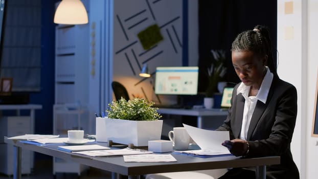 African american black woman working hard late at night in office meeting room checking company financial graphs. Focused manager drinking coffee analyzing management statistics presentation