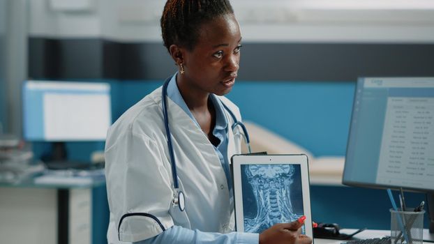 Close up of medic pointing at tablet display with radiography, analyzing bones structure and healthcare diagnosis in cabinet. Doctor holding modern gadget with x ray scan on screen.