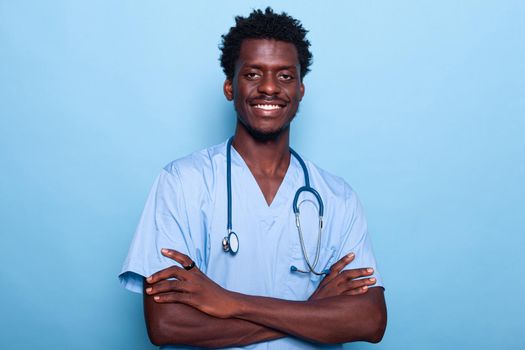 Portrait of man nurse wearing uniform and stethoscope over isolated background. Medical assistant standing with crossed arms and looking at camera in studio. Confident healthcare specialist