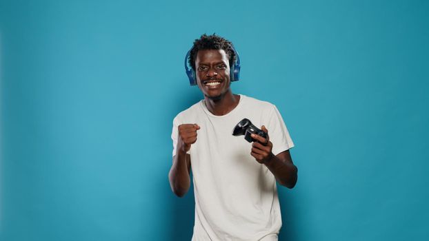 Happy man winning at video games with joystick on console. Cheerful person playing online game using wireless controller for virtual entertainment. Gamer with headphones enjoying play