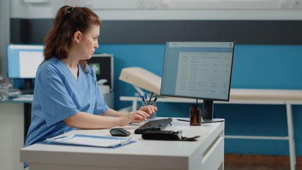 Nurse typing on computer keyboard for consultation and appointment. Medical assistant using technology for healthcare system in doctors office. Specialist working with medical equipment