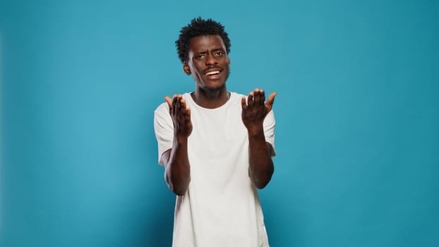 Casual person talking and using hands to applaud in studio. Young man looking at camera with smile and applauding, saying congratulations over isolated background. Positive adult clapping