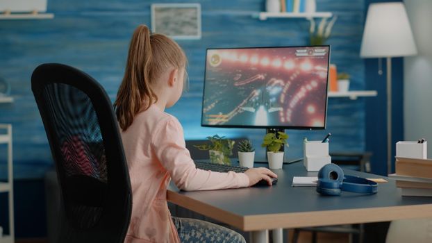 Young child playing action video games on computer at desk. Little girl losing at futuristic shooting game on monitor. Player gaming for fun and entertainment after online classes