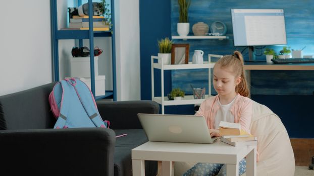 Little child using laptop for online school classes at home. Schoolgirl looking at display of modern device for homework and remote education. Young pupil learning courses on internet