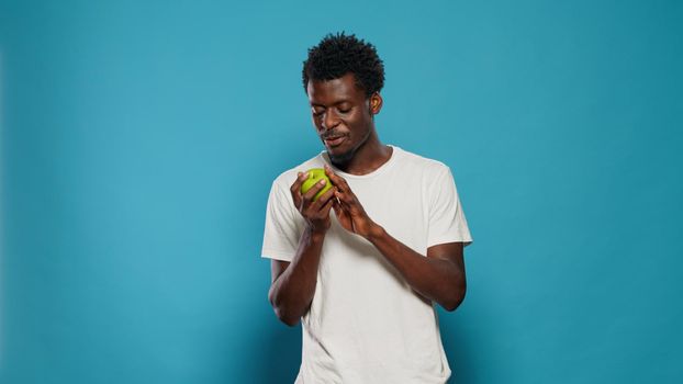Vegetarian man playing with green apple in studio. Joyful person throwing fruits, feeling excited about healthy diet and nutrition. Adult looking at camera and presenting snack with vitamins