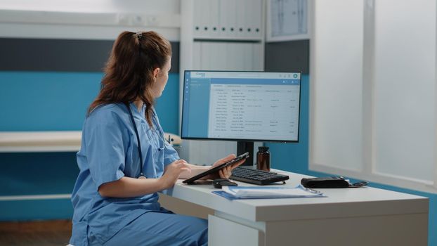 Medical assistant working with computer and digital tablet for healthcare system and appointments. Woman nurse holding device with touch screen in doctors office for annual checkup visit.