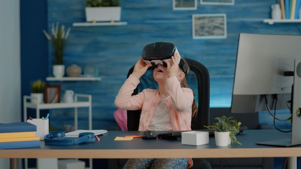 Little child studying with vr glasses for homework and online classes at desk. Young girl with headset preparing for school remote courses and lessons at home. Schoolgirl with technology